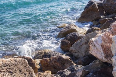 Dalgalar halinde akan turkuaz deniz suyuyla kayalık kıyılar ve kalın beyaz deniz köpüğü oluşturur..