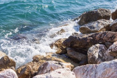 Deniz dalgaları kayalık kıyıya yuvarlanır ve büyük kayalara çarpar, köpük oluşturur..
