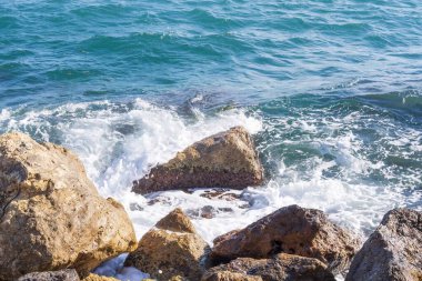 Dalgalar halinde akan turkuaz deniz suyuyla kayalık kıyılar ve kalın beyaz deniz köpüğü oluşturur..