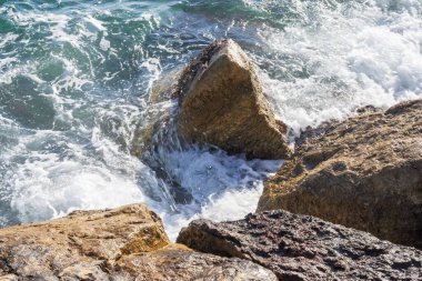 Deniz dalgaları kayalık kıyıya yuvarlanır ve büyük kayalara çarpar, köpük oluşturur..