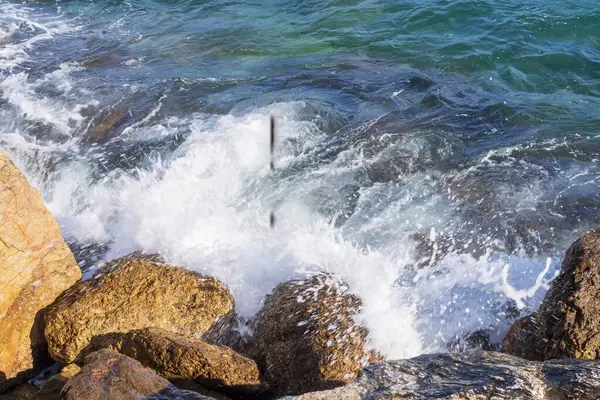 Deniz dalgaları kayalık kıyıya yuvarlanır ve büyük kayalara çarpar, köpük oluşturur..