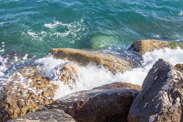 Deniz dalgaları kayalık kıyıya yuvarlanır ve büyük kayalara çarpar, köpük oluşturur..