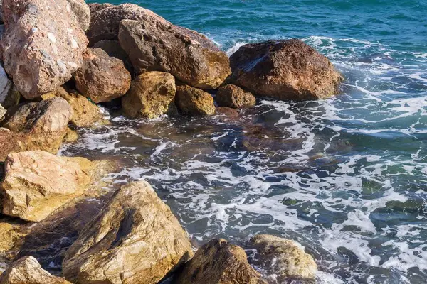 Dalgalar halinde akan turkuaz deniz suyuyla kayalık kıyılar ve kalın beyaz deniz köpüğü oluşturur..