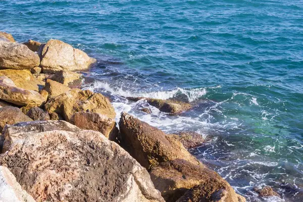 Deniz dalgaları kayalık kıyıya yuvarlanır ve büyük kayalara çarpar, köpük oluşturur..