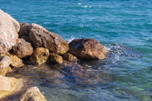 Dalgalar halinde akan turkuaz deniz suyuyla kayalık kıyılar ve kalın beyaz deniz köpüğü oluşturur..