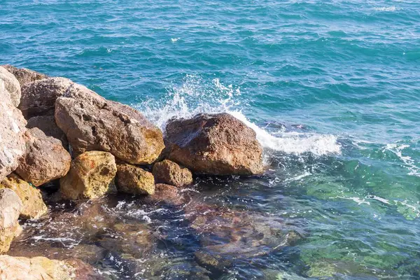 Deniz dalgaları kayalık kıyıya yuvarlanır ve büyük kayalara çarpar, köpük oluşturur..