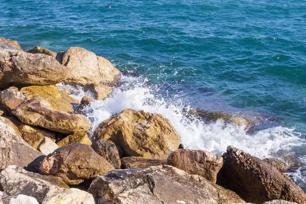 Deniz dalgaları kayalık kıyıya yuvarlanır ve büyük kayalara çarpar, köpük oluşturur..