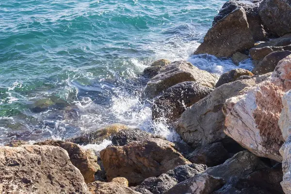 Deniz dalgaları kayalık kıyıya yuvarlanır ve büyük kayalara çarpar, köpük oluşturur..