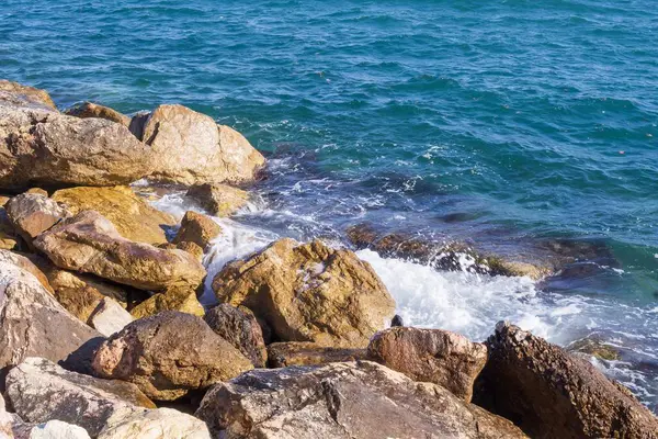 Dalgalar halinde akan turkuaz deniz suyuyla kayalık kıyılar ve kalın beyaz deniz köpüğü oluşturur..