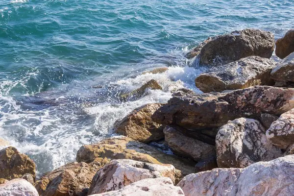 Deniz dalgaları kayalık kıyıya yuvarlanır ve büyük kayalara çarpar, köpük oluşturur..