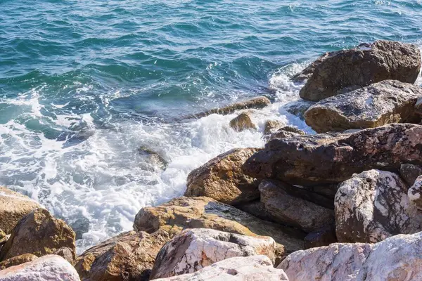 Dalgalar halinde akan turkuaz deniz suyuyla kayalık kıyılar ve kalın beyaz deniz köpüğü oluşturur..