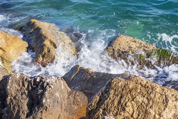 Deniz dalgaları kayalık kıyıya yuvarlanır ve büyük kayalara çarpar, köpük oluşturur..
