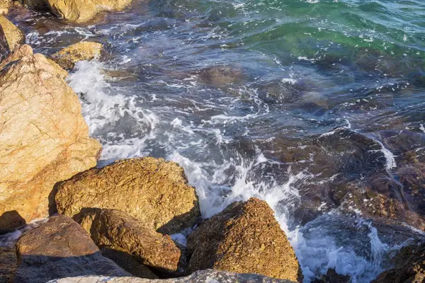Dalgalar halinde akan turkuaz deniz suyuyla kayalık kıyılar ve kalın beyaz deniz köpüğü oluşturur..