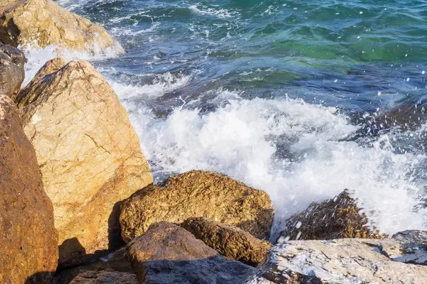 Deniz dalgaları kayalık kıyıya yuvarlanır ve büyük kayalara çarpar, köpük oluşturur..