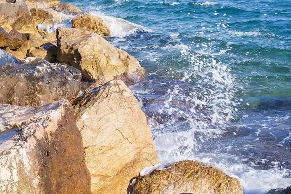 Deniz dalgaları kayalık kıyıya yuvarlanır ve büyük kayalara çarpar, köpük oluşturur..