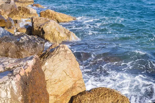 Dalgalar halinde akan turkuaz deniz suyuyla kayalık kıyılar ve kalın beyaz deniz köpüğü oluşturur..