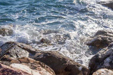 Dalgalar halinde akan turkuaz deniz suyuyla kayalık kıyılar ve kalın beyaz deniz köpüğü oluşturur..