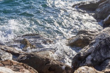 Gün batımında çakıl taşlı kıyılarda köpüklü deniz dalgaları.