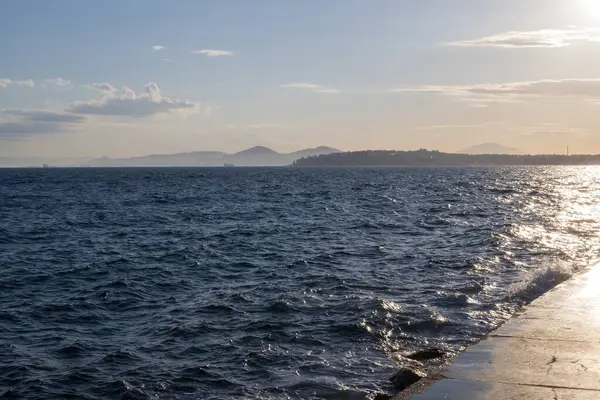 Gün batımında çakıl taşlı kıyılarda köpüklü deniz dalgaları.
