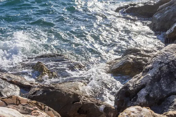 Gün batımında çakıl taşlı kıyılarda köpüklü deniz dalgaları.