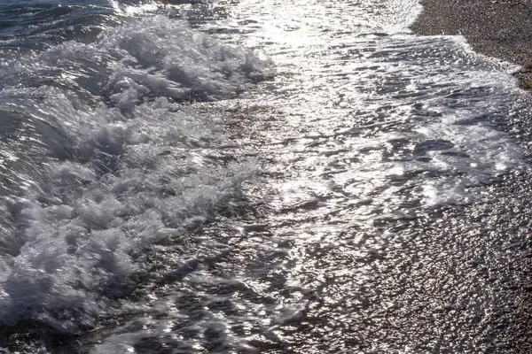 Gün batımında çakıl taşlı kıyılarda köpüklü deniz dalgaları.