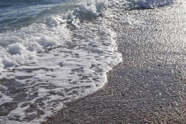 Gün batımında çakıl taşlı kıyılarda köpüklü deniz dalgaları.