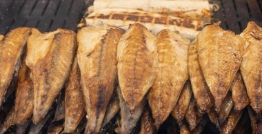 Geleneksel Türk sokak yemeği Balik ekmek 'i hazırlama süreci. Izgara uskumru balığı filetosu bir sokak yiyecek pazarında açık kömür ızgarasında pişiyor ve sebzeli pide ekmeğine sarılıyor..