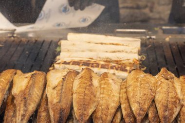 Geleneksel Türk sokak yemeği Balik ekmek 'i hazırlama süreci. Izgara uskumru balığı filetosu bir sokak yiyecek pazarında açık kömür ızgarasında pişiyor ve sebzeli pide ekmeğine sarılıyor..