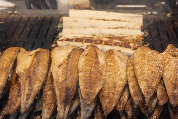 Geleneksel Türk sokak yemeği Balik ekmek 'i hazırlama süreci. Izgara uskumru balığı filetosu bir sokak yiyecek pazarında açık kömür ızgarasında pişiyor ve sebzeli pide ekmeğine sarılıyor..