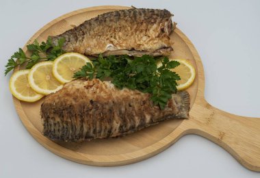 Tahta tahtada taze limon dilimleri ve maydanozlu garnitürle servis edilen kızarmış balık.