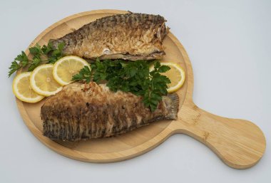 Tahta tahtada taze limon dilimleri ve maydanozlu garnitürle servis edilen kızarmış balık.