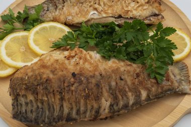 Tahta tahtada taze limon dilimleri ve maydanozlu garnitürle servis edilen kızarmış balık.