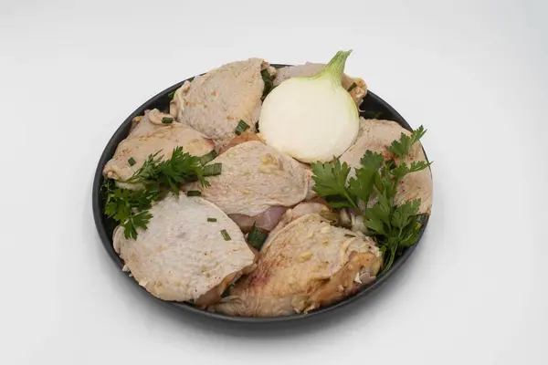 Çiğ tavuk butları, sarımsaklı ve yeşil soğanlı siyah kasede beyaz arka planda. Et barbekü için hazır.