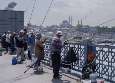 İstanbul, Trkiye 'deki Galata Köprüsü' nde camiler ve arka planda ufuk çizgisi olan bir grup balıkçı balık tutuyor. İstanbul, 20 Mayıs 2025