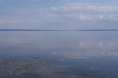 Sakin nehir manzarası yumuşak akşam ışığı ve bulutlar suda yansıyor.