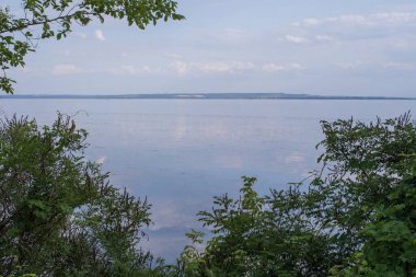 Sakin nehir manzarası yumuşak akşam ışığı ve bulutlar suda yansıyor.