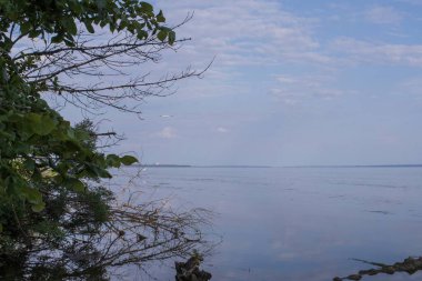 Sakin nehir manzarası yumuşak akşam ışığı ve bulutlar suda yansıyor.