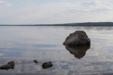 Sakin nehir manzarası yumuşak akşam ışığı ve bulutlar suda yansıyor.