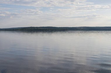 Sakin nehir manzarası yumuşak akşam ışığı ve bulutlar suda yansıyor.