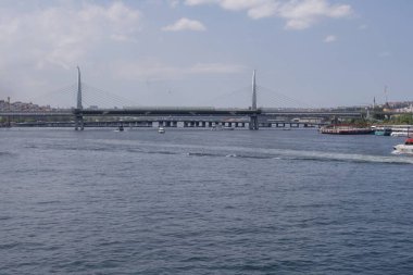 İstanbul 'daki Golden Horn Metro Köprüsü' nün sakin sularda hareket eden yolcu tekneleriyle geniş görüşü var. Şehir nehir manzarası modern köprü mimarisi, şehir silüeti ve güneşli bir günde açık gökyüzü.