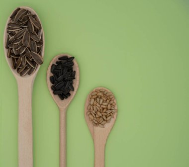 Üç tip ayçekirdeğinin yatay görüntüsü. Kabuklu ve ahşap kaşıklarda kızartılmış yeşil zemin üzerinde. Doğal çerez ve tarım teması.