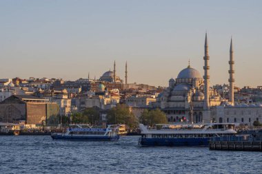 İstanbul 'daki Yeni Cami camii üzerinde günbatımında, Boğaz boyunca geleneksel feribotlar dolaşıyor. Osmanlı mimarisi ve Türk kültür başkentinin kentsel manzarası. İstanbul 20 Mayıs 2025