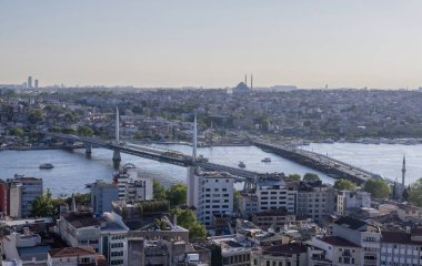İstanbul 'daki Haliç Köprüsü' nü feribot, eski binalar ve arka planda tarihi Valens Su kemeri ile geçen modern Hali Metro Köprüsü. 20 Mayıs 2025 'te gün batımında yakalandılar..
