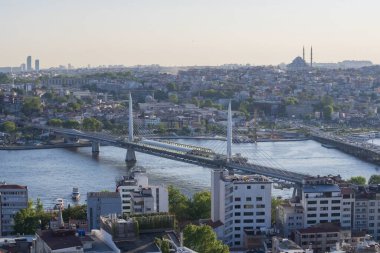 İstanbul 'daki Haliç Köprüsü' nü feribot, eski binalar ve arka planda tarihi Valens Su kemeri ile geçen modern Hali Metro Köprüsü. 20 Mayıs 2025 'te gün batımında yakalandılar..