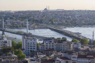 İstanbul 'daki Haliç Köprüsü' nü feribot, eski binalar ve arka planda tarihi Valens Su kemeri ile geçen modern Hali Metro Köprüsü. 20 Mayıs 2025 'te gün batımında yakalandılar..