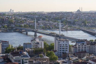 İstanbul 'daki Haliç Köprüsü' nü feribot, eski binalar ve arka planda tarihi Valens Su kemeri ile geçen modern Hali Metro Köprüsü. 20 Mayıs 2025 'te gün batımında yakalandılar..