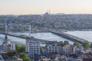 İstanbul 'daki Haliç Köprüsü' nü feribot, eski binalar ve arka planda tarihi Valens Su kemeri ile geçen modern Hali Metro Köprüsü. 20 Mayıs 2025 'te gün batımında yakalandılar..