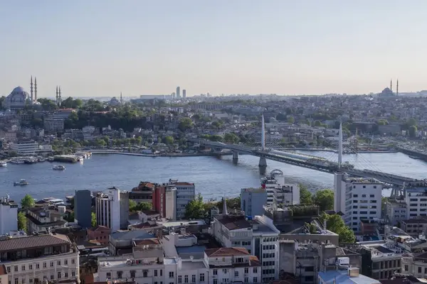 İstanbul 'daki Haliç Köprüsü' nü feribot, eski binalar ve arka planda tarihi Valens Su kemeri ile geçen modern Hali Metro Köprüsü. 20 Mayıs 2025 'te gün batımında yakalandılar..