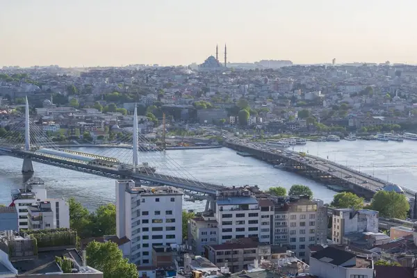 İstanbul 'daki Haliç Köprüsü' nü feribot, eski binalar ve arka planda tarihi Valens Su kemeri ile geçen modern Hali Metro Köprüsü. 20 Mayıs 2025 'te gün batımında yakalandılar..