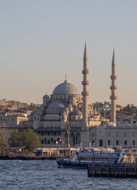 İstanbul 'daki Yeni Cami camii üzerinde günbatımında, Boğaz boyunca geleneksel feribotlar dolaşıyor. Osmanlı mimarisi ve Türk kültür başkentinin kentsel manzarası. İstanbul 20 Mayıs 2025